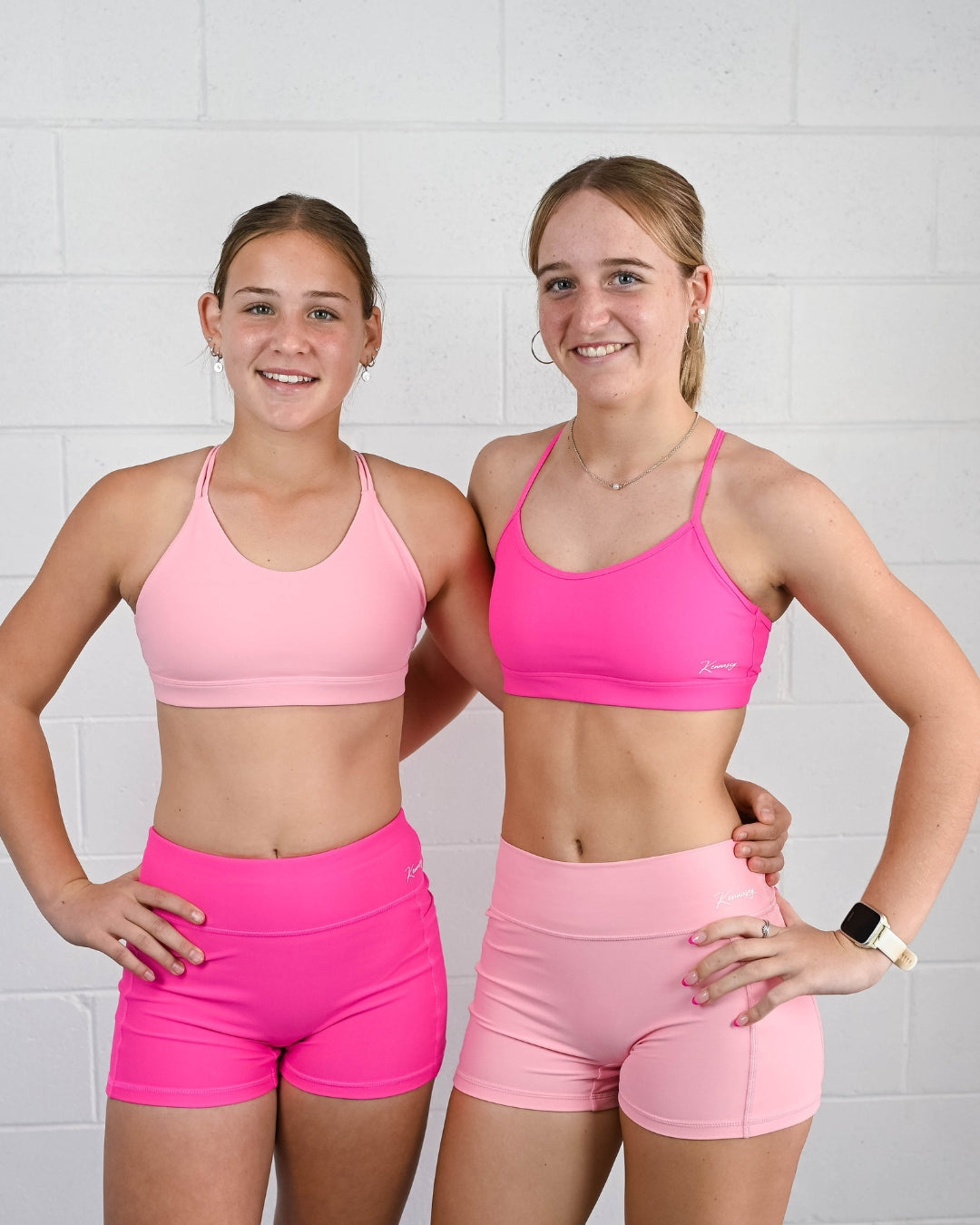 Two girls wearing pink Kennasey activewear sets with Active and Momentum bike shorts, showing different waistband styles.